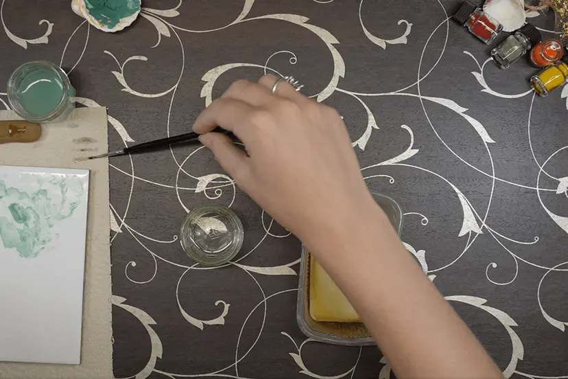 Nettoyage d’un pinceau au savon, godets de couleur et flacons de pigments sur la table d’atelier